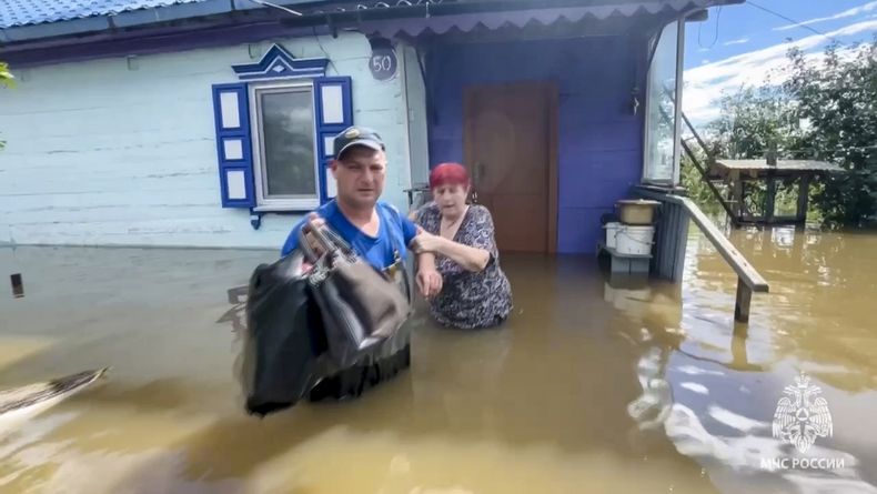 In this photo, taken from a video released by the Russian Emergencies Ministry Press Service on Sunday, August 13, 2023, an emergency service worker helps a woman to get out of her home in a flooded village in the region of Primorye, in the Russian Far East, after heavy downpours inundated villages in the region following Typhoon Khanun.  (Press Service of the Ministry of Emergencies via AP)