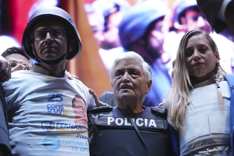 Wearing a bulletproof vest and helmet, presidential hopeful Christian Zurita, left, and his partner Andrea González, right, with Gloria Valencia, center, mother of slain candidate Fernando Villavicencio, present themselves to their supporters at the closing ceremony of the campaign in Quito, Ecuador, on Thursday, August 17, 2023. The early elections on August 20 were called after President Guillermo Lasso dissolved the National Assembly in May to avoid impeachment against him .  (AP Photo/Dolores Ochoa)