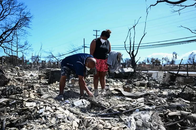 Una pareja regresa a las ruinas de su hogar en Lahaina, al este de Maui, luego de los siniestros en este condado. Foto Afp