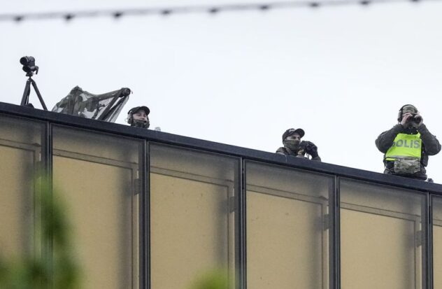 Police officers watch from a rooftop as people line up for the second dress rehearsal of the first semi-final of the Eurovision Song Contest in Malmo, Sweden, Monday, May 6, 2024.
