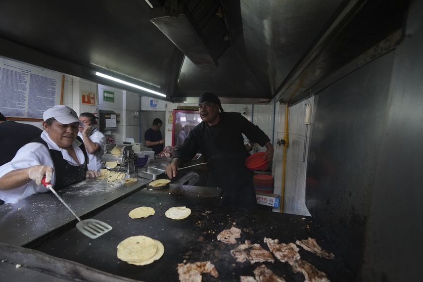 Chef Arturo Rivera Martínez, recently awarded a Michelin star, grabs several plates while an assistant heats corn tortillas on a griddle at the Tacos El Califa de León taco shop in Mexico City, Wednesday, May 15, 2024. Tacos El Califa de Len is the first taqueria to receive a Michelin star.