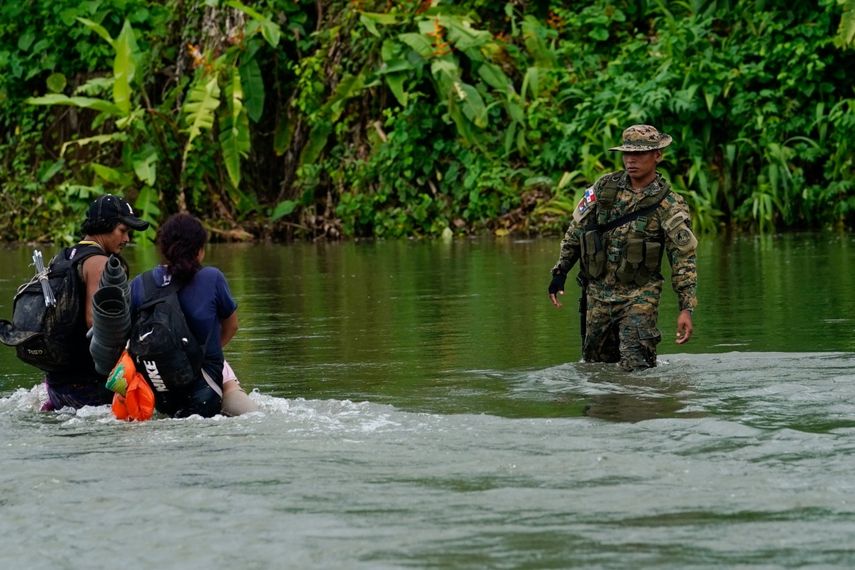 A Panamanian border agent looks on as two migrants cross the Tuquesa River after walking through the Darien Gap, in Bajo Chiquito, Panama, on October 4, 2023. 
